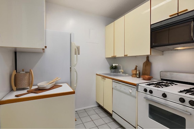 kitchen with light tile patterned flooring, sink, cream cabinets, and white appliances