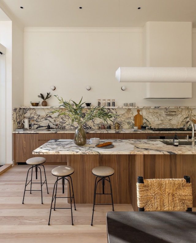 kitchen with light wood-style flooring, ornamental molding, brown cabinets, and a breakfast bar area