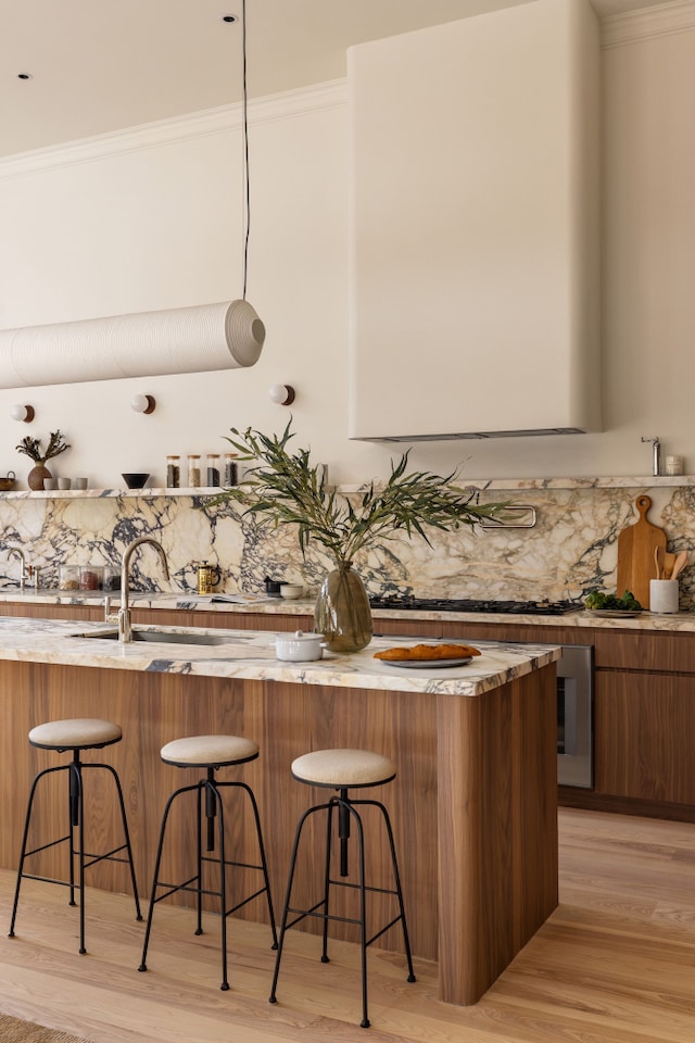 bar with a sink, light wood-style floors, decorative backsplash, wet bar, and crown molding