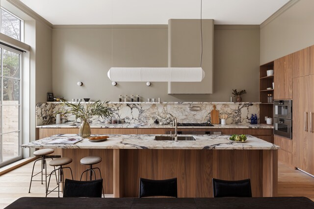 kitchen featuring pendant lighting, sink, a towering ceiling, stainless steel appliances, and light wood-type flooring