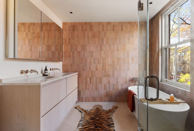 bathroom with a freestanding bath, vanity, tile patterned flooring, and tile walls