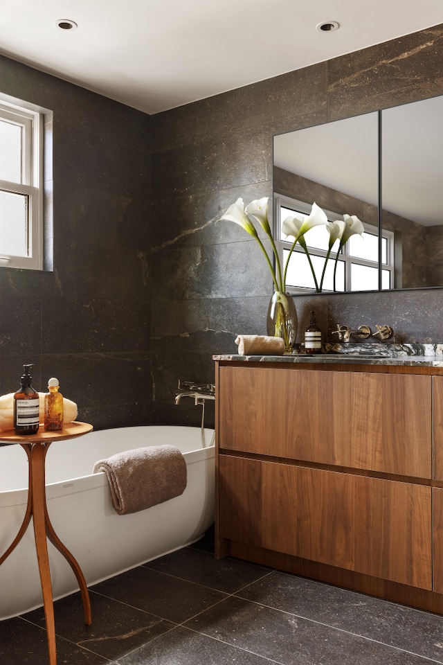 full bathroom featuring plenty of natural light, a soaking tub, granite finish floor, and vanity