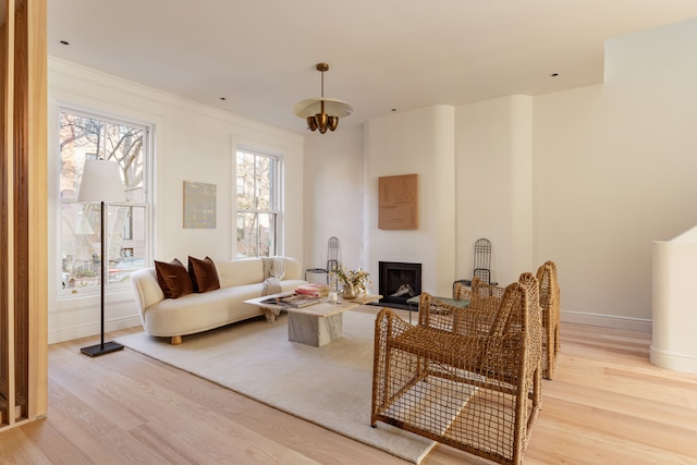 living room with baseboards, crown molding, a fireplace, and light wood-style floors