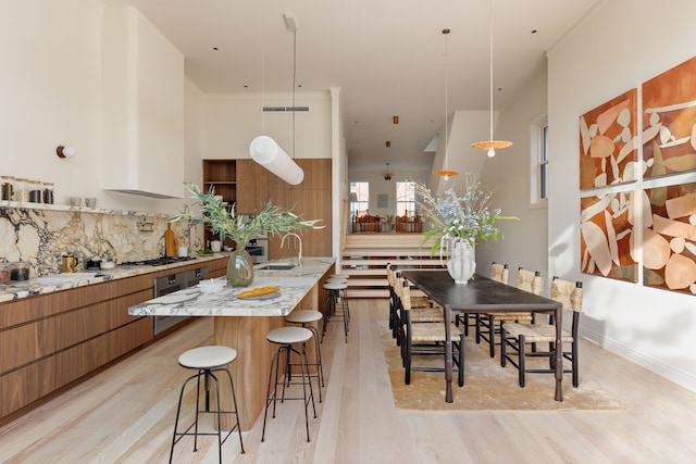 kitchen with a breakfast bar area, decorative backsplash, brown cabinetry, a sink, and modern cabinets