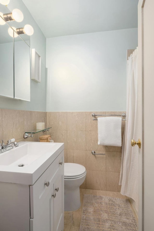 bathroom with tile walls, toilet, vanity, and a wainscoted wall
