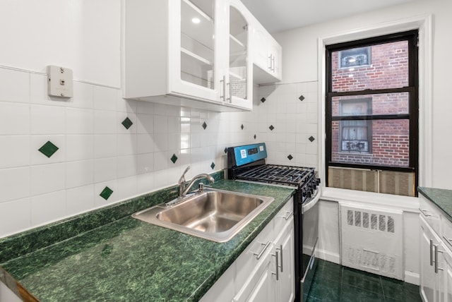 kitchen with dark countertops, radiator, glass insert cabinets, stainless steel range with gas stovetop, and a sink