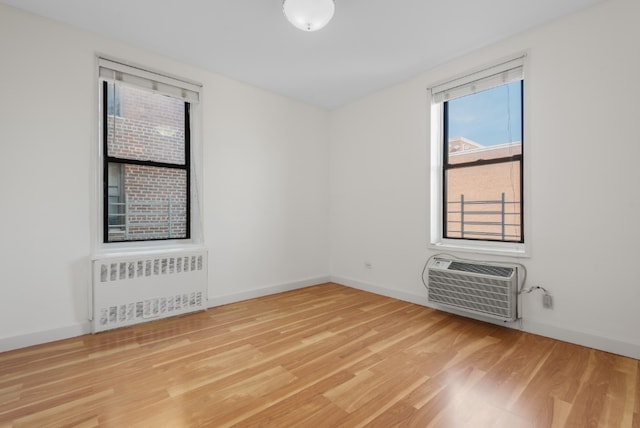 empty room with radiator, a wall unit AC, baseboards, and light wood finished floors