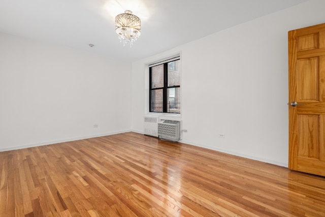 unfurnished room featuring an AC wall unit, radiator, a chandelier, and light hardwood / wood-style flooring