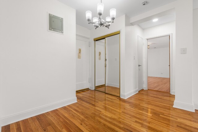 unfurnished bedroom with light wood finished floors, a notable chandelier, baseboards, and a closet