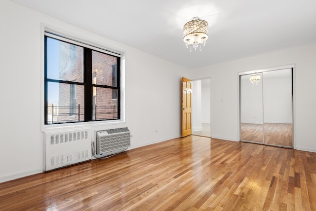 unfurnished bedroom featuring radiator, a wall mounted AC, a notable chandelier, and light hardwood / wood-style flooring