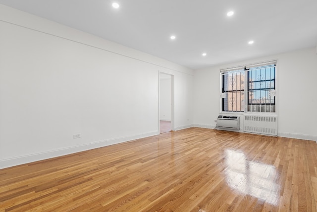 empty room with radiator, light wood-style flooring, baseboards, and recessed lighting