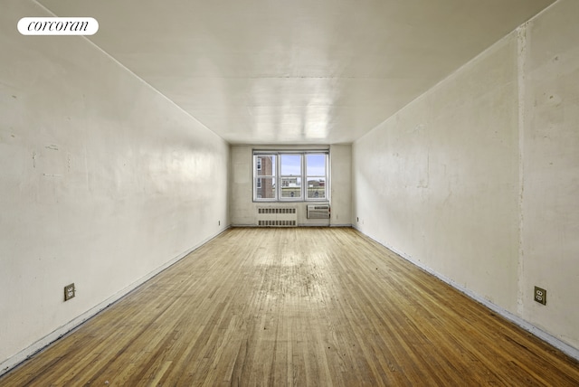 unfurnished room with radiator heating unit, visible vents, hardwood / wood-style floors, and a wall mounted air conditioner