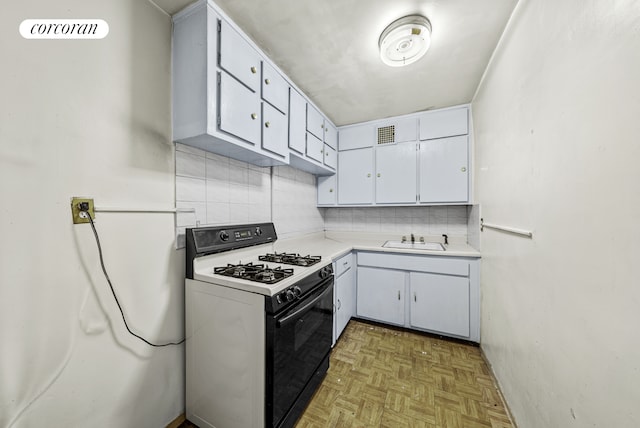 kitchen with decorative backsplash, gas range oven, light countertops, white cabinetry, and a sink