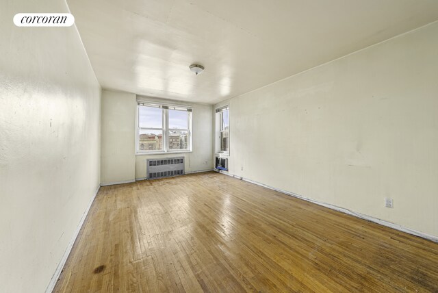 spare room with wood-type flooring, visible vents, and radiator heating unit