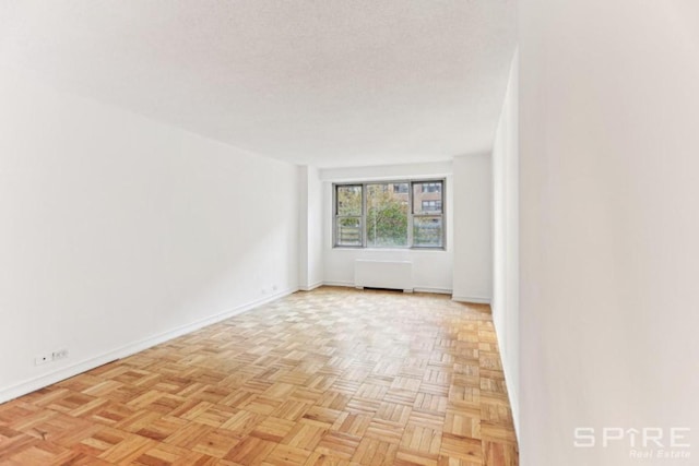 empty room with light parquet flooring, a textured ceiling, and radiator heating unit