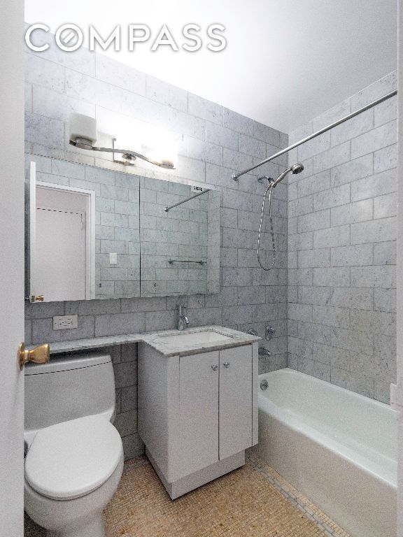 full bathroom featuring vanity, tiled shower / bath combo, toilet, and tile walls