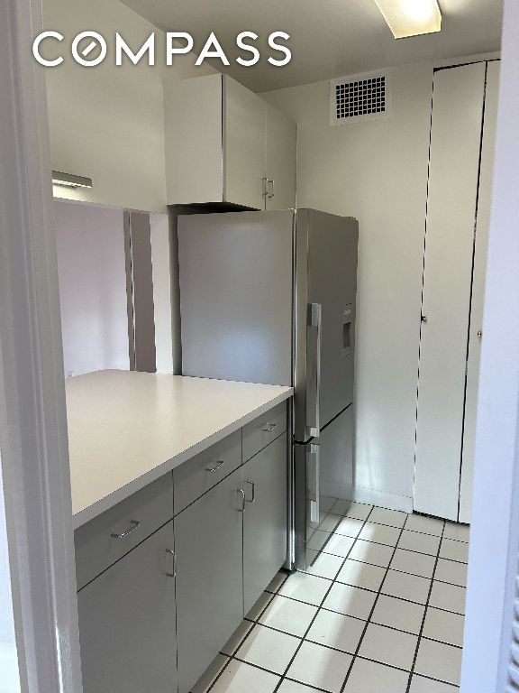 kitchen with light tile patterned floors, visible vents, light countertops, gray cabinets, and stainless steel fridge