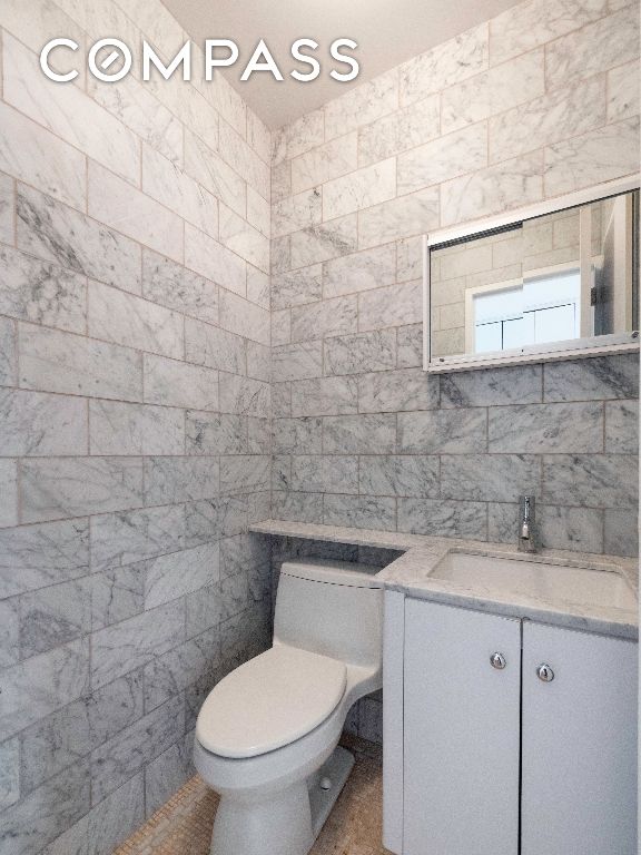 bathroom featuring vanity, toilet, and tile walls