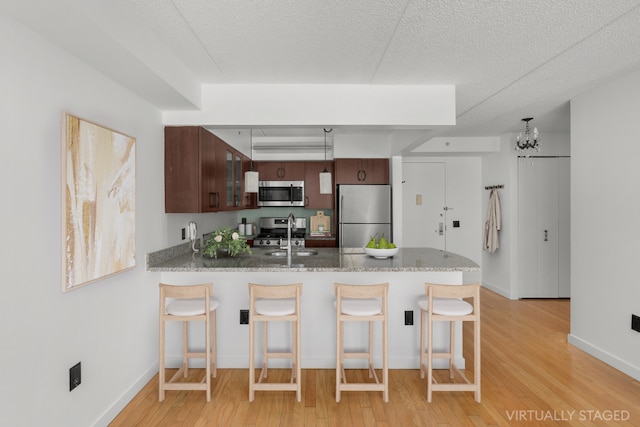 kitchen with a kitchen bar, kitchen peninsula, stainless steel appliances, dark brown cabinets, and light wood-type flooring