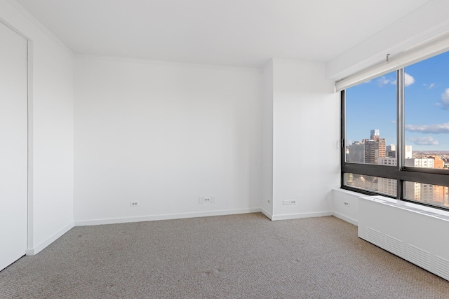 unfurnished room with carpet floors, baseboards, a city view, and crown molding
