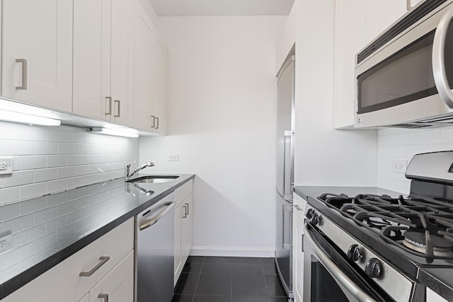 kitchen featuring appliances with stainless steel finishes, a sink, dark countertops, dark tile patterned floors, and white cabinetry