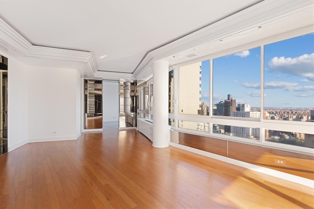 empty room with wood finished floors, a view of city, baseboards, and crown molding