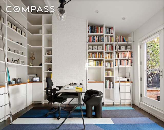 home office featuring wood finished floors and brick wall