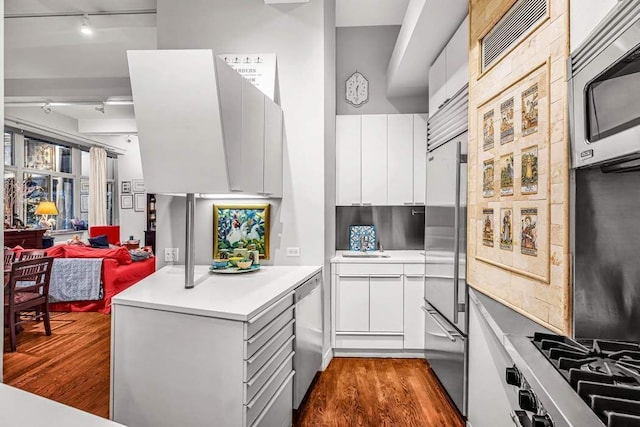 kitchen with appliances with stainless steel finishes, track lighting, dark wood-type flooring, white cabinetry, and sink