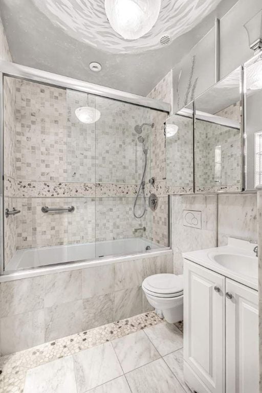 full bathroom with vanity, toilet, bath / shower combo with glass door, and tile walls