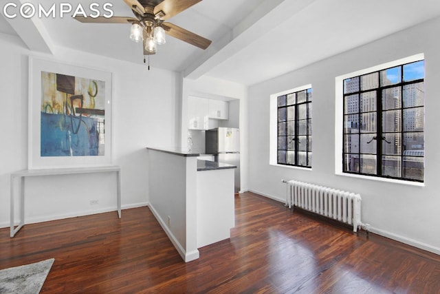 interior space featuring ceiling fan, dark hardwood / wood-style floors, radiator, white cabinets, and beamed ceiling