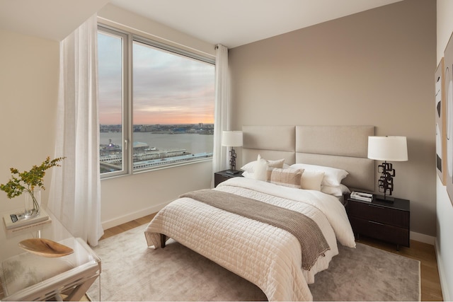bedroom with multiple windows, wood finished floors, and baseboards