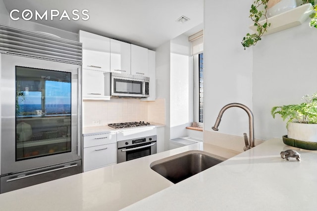 kitchen with a sink, white cabinetry, light countertops, appliances with stainless steel finishes, and backsplash