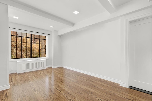 empty room with beamed ceiling, radiator heating unit, and light hardwood / wood-style flooring