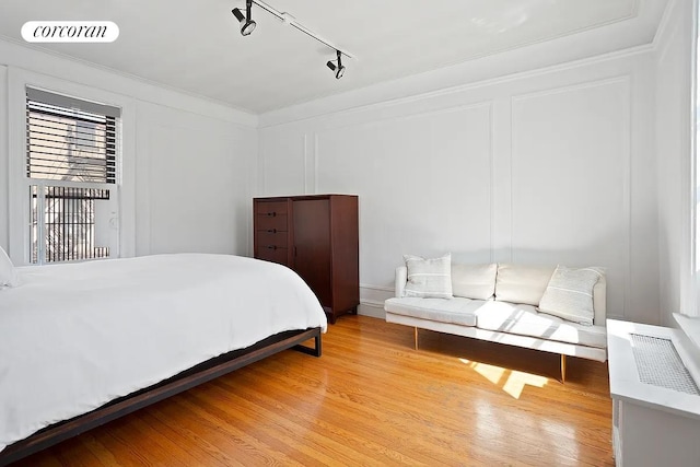 bedroom with crown molding, light wood-type flooring, visible vents, and a decorative wall