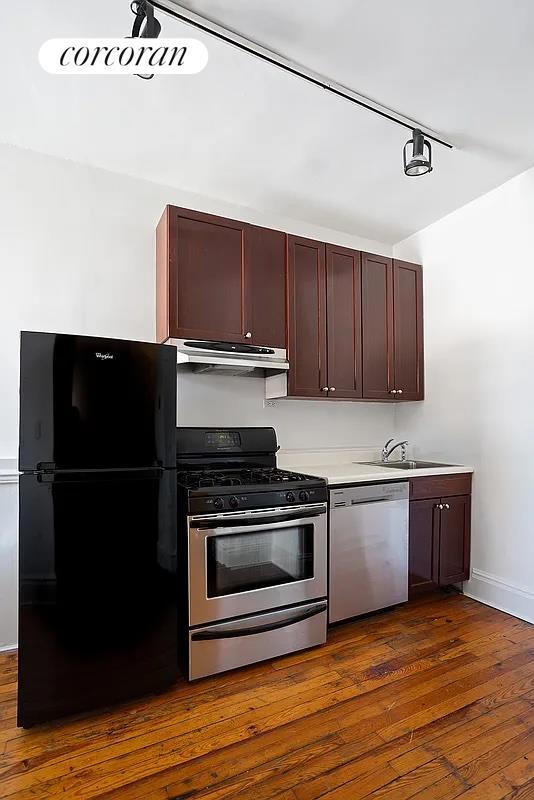 kitchen featuring under cabinet range hood, a sink, light countertops, appliances with stainless steel finishes, and dark wood finished floors