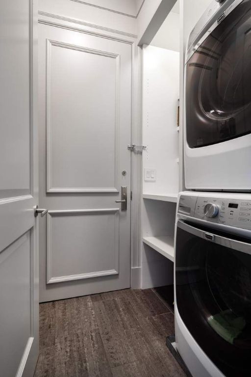 laundry area with stacked washer and clothes dryer and dark hardwood / wood-style flooring