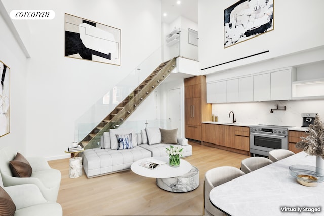 living room featuring a high ceiling, light wood-style floors, stairs, and visible vents