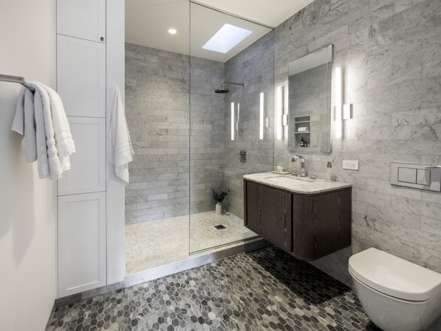 bathroom with tile walls, vanity, a skylight, tiled shower, and toilet