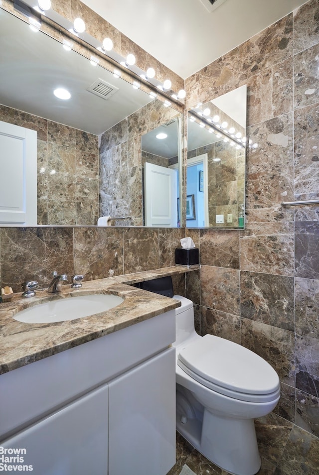 half bathroom with vanity, toilet, marble finish floor, tile walls, and visible vents