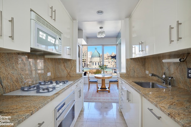 kitchen with white appliances, white cabinetry, light stone counters, and a sink