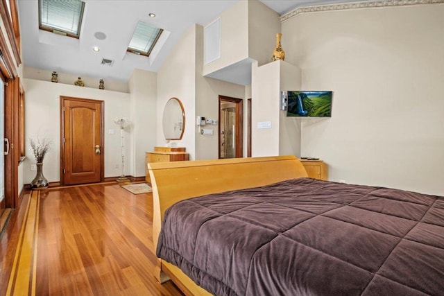 bedroom featuring wood-type flooring, a skylight, and high vaulted ceiling