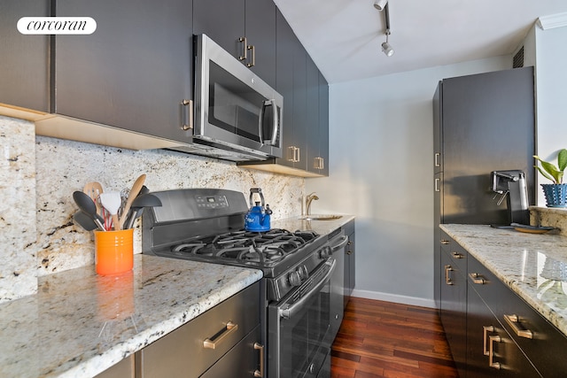 kitchen with light stone counters, dark wood finished floors, tasteful backsplash, appliances with stainless steel finishes, and a sink