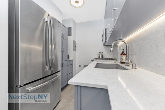 kitchen featuring stainless steel refrigerator, light stone countertops, sink, and gray cabinetry