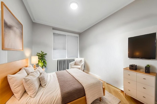 bedroom with crown molding, radiator heating unit, and light hardwood / wood-style flooring