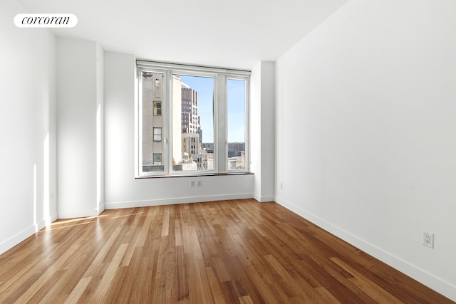 empty room with baseboards, light wood finished floors, visible vents, and a city view