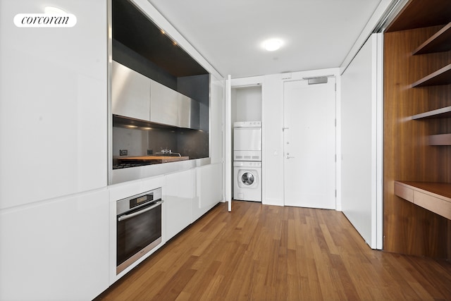 kitchen featuring oven, a fireplace, light wood-type flooring, stacked washing maching and dryer, and modern cabinets