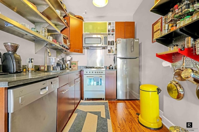 kitchen with appliances with stainless steel finishes, dark countertops, a sink, and open shelves