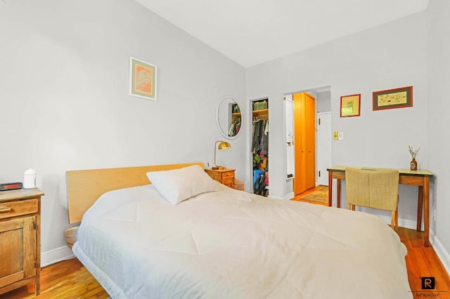 bedroom with a closet, light wood-type flooring, a walk in closet, and baseboards