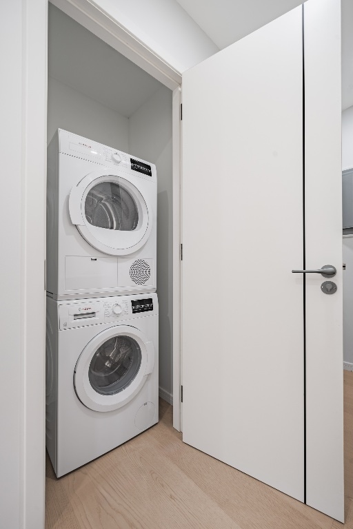 clothes washing area with stacked washer and clothes dryer and light wood-type flooring