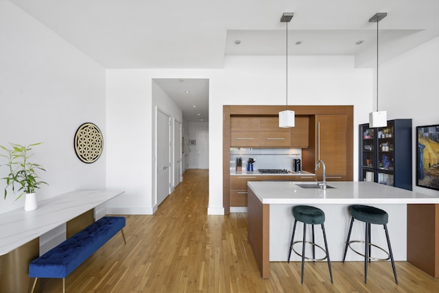 kitchen featuring a kitchen bar, sink, decorative light fixtures, a center island with sink, and light wood-type flooring